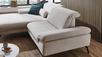 Detailaufnahme einer modernen hellen Stoffcouch mit verstellbaren Armlehnen und weichen Polstern, platziert auf warmem Holzfußboden mit Akzentwand aus Holzlamellen – kombiniert Komfort mit elegantem, zeitlosem Design.